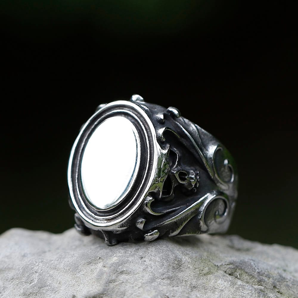 Front three-quarter view of men's Gothic skull signet ring in 316L stainless steel resting on a stone