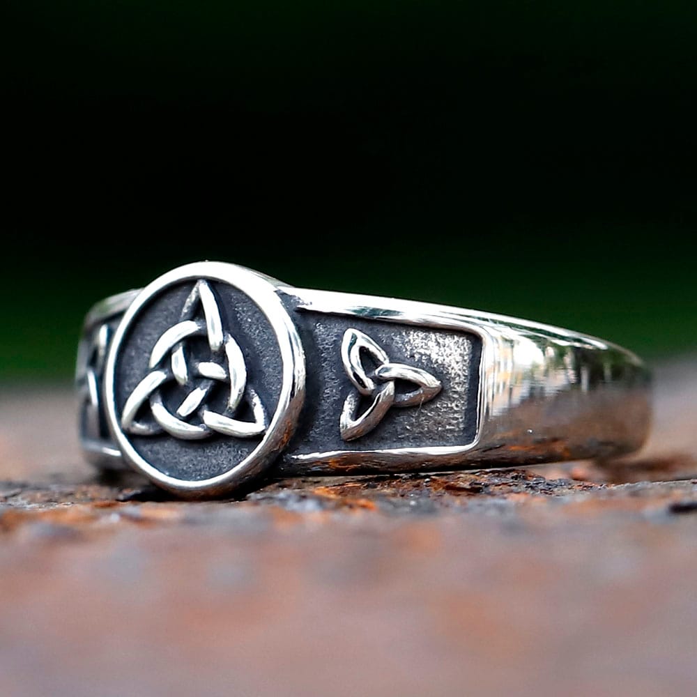 Close-up of a stainless steel Celtic Triquetra knot ring with an antiqued finish on a dark, rustic background.