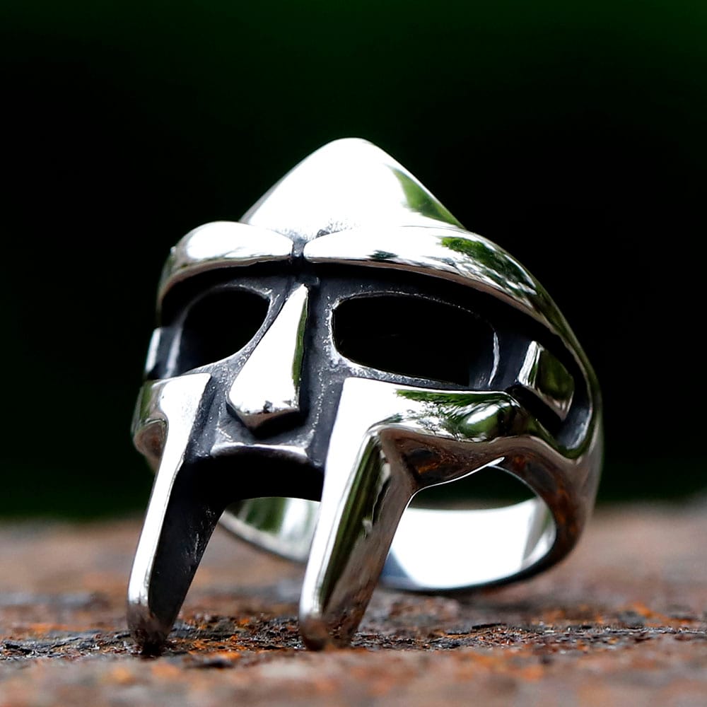 Close-up of the polished stainless steel MF Doom mask ring on a textured dark background.