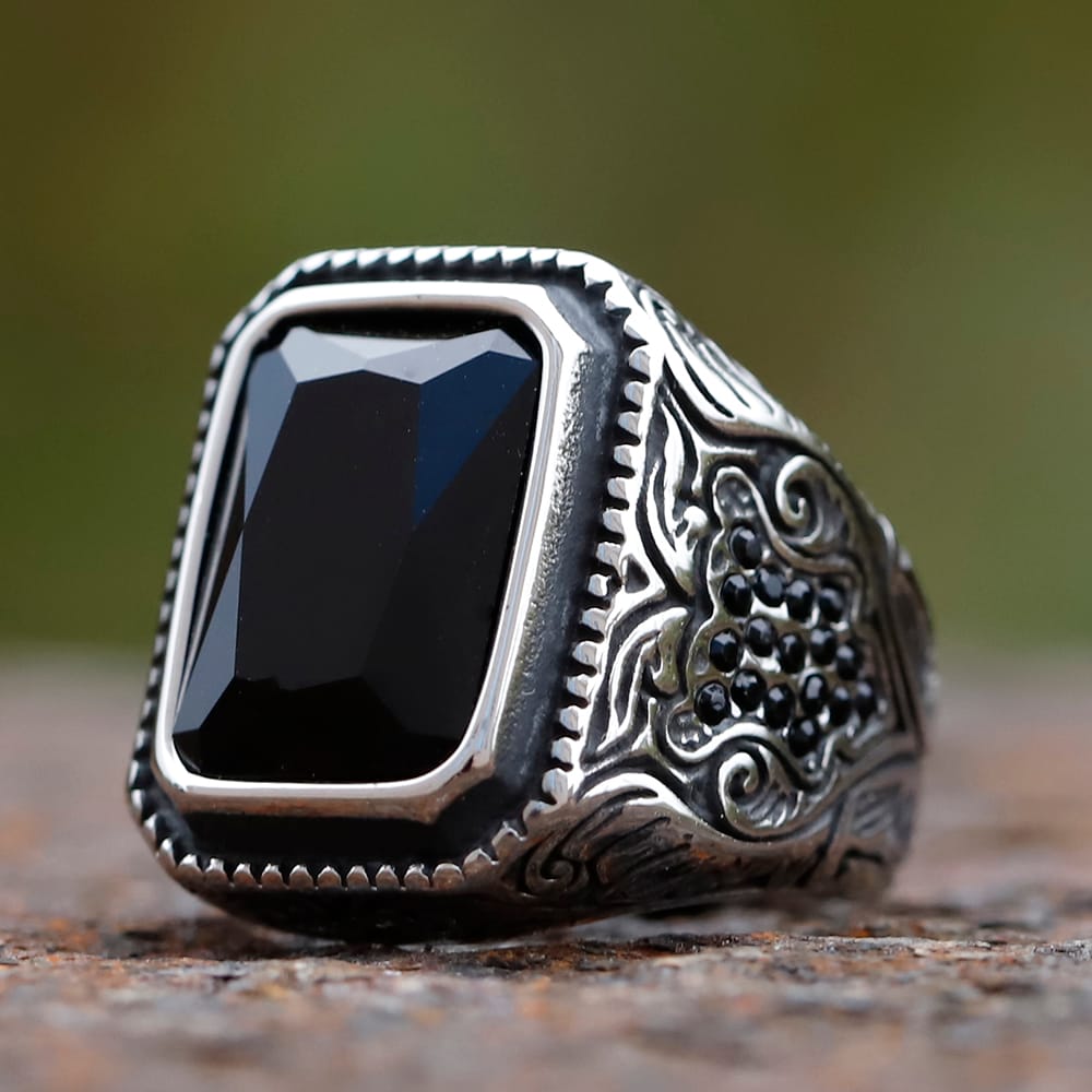 Three-quarter view of men's stainless steel signet ring featuring a faceted rectangular black stone and ornate filigree engraving