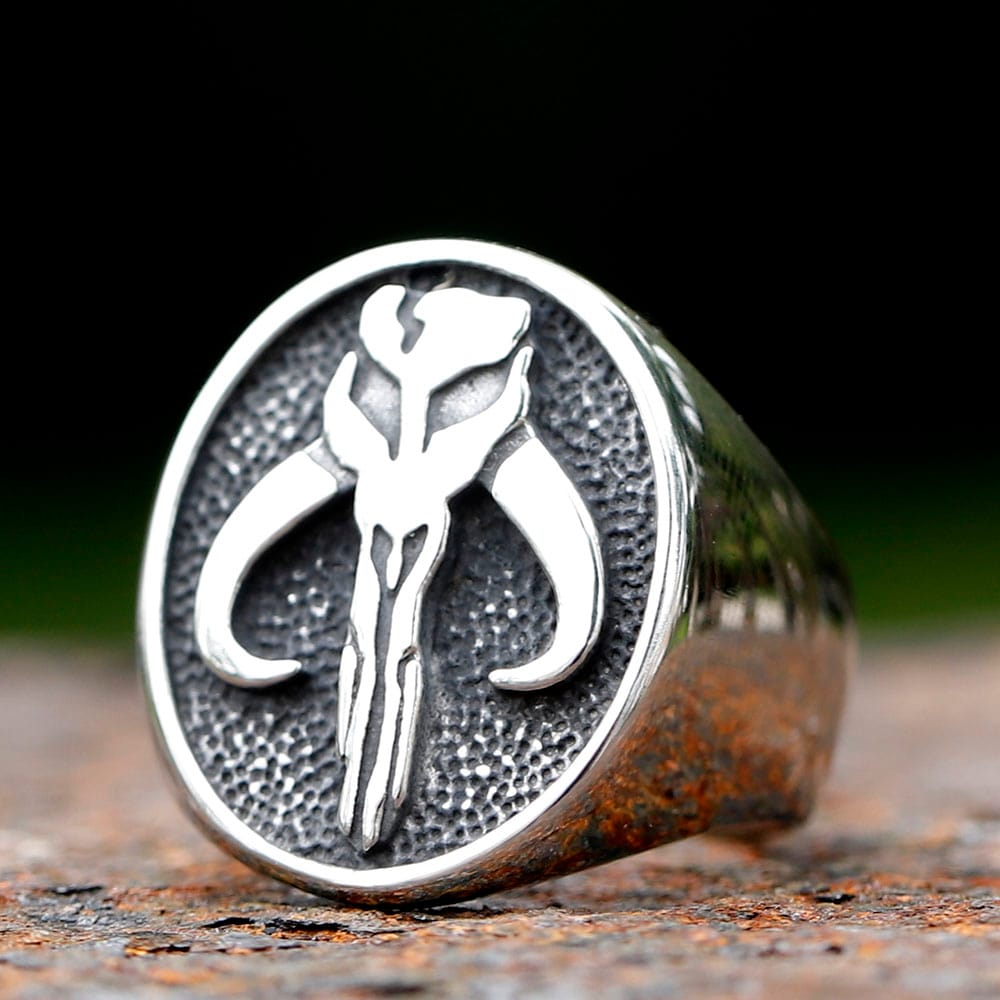 Close-up of the Mythosaur skull emblem on the stainless steel ring with a dark, blurred background.