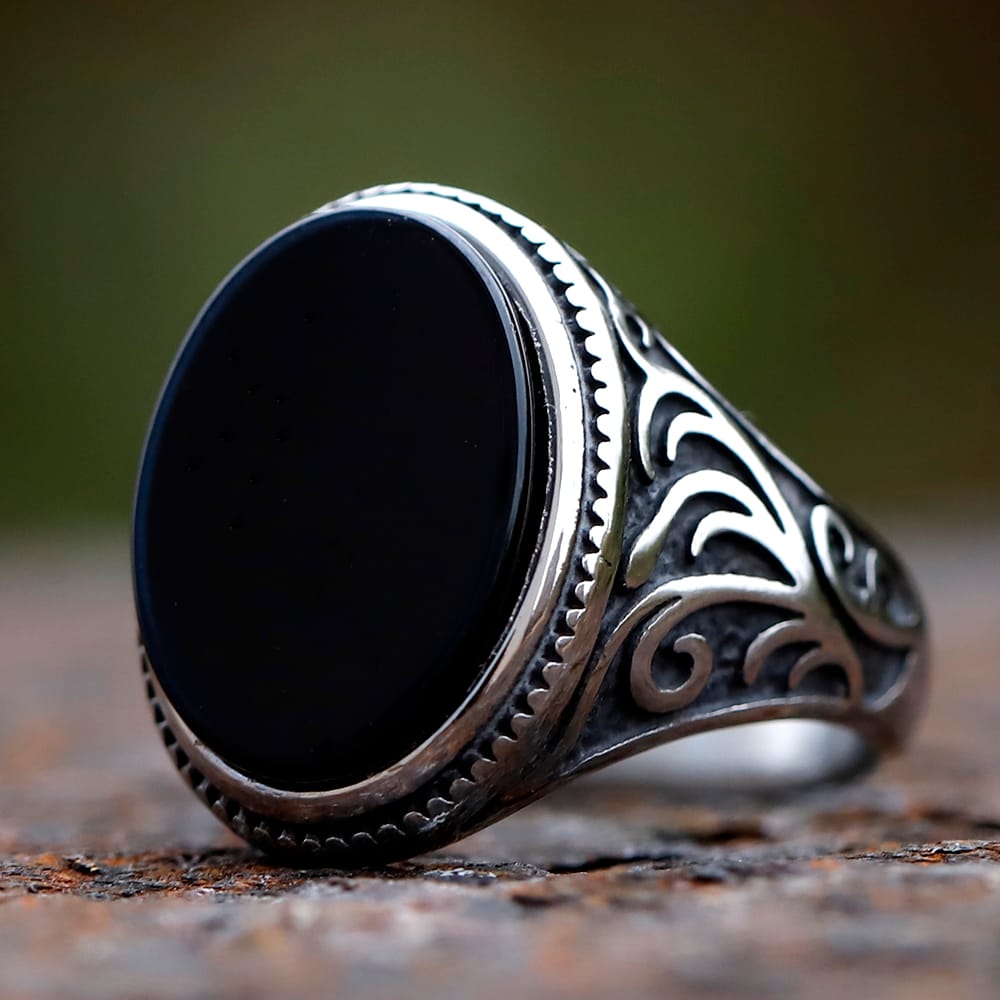 Close-up of men's retro silver ring with prominent oval black stone and intricate band carving