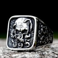Square-faced 316L stainless steel ring featuring a detailed skull relief surrounded by swirling organic patterns on the face and sides, with polished raised areas and darkened recesses.