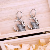 Pair of stainless steel Viking howling wolf and crescent moon drop earrings resting in a wooden jewelry box