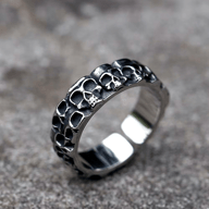 316L stainless steel band ring with an exterior entirely covered in dark, detailed skull designs and a smooth, polished interior, on a grey textured background.