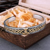 Stainless steel Viking cuff bracelet featuring gold-tone Thor's Hammer and Celtic knotwork resting on a wooden box