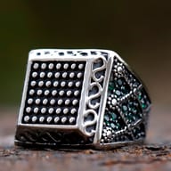 Front three-quarter angle of square stainless steel signet ring with green zircon accents