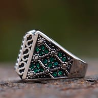 Side profile showing carved scrollwork engraving and inset green stones on a steel ring