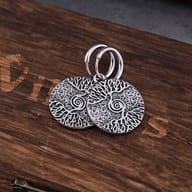 Pair of Viking Tree of Life stainless steel hoop earrings resting on a rustic wooden surface.