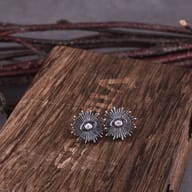 Top-down view of gothic celestial sunburst eye earrings on a dark textured background