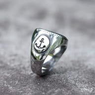 Side profile of the 316L stainless steel ring, showcasing the anchor motif and textured band detail, on a grey rock.