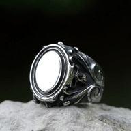 Antiqued stainless steel gothic skull ring featuring a polished oval surface and detailed skull and scrollwork on the band, displayed on a rock.
