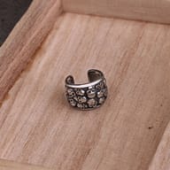 Stainless steel skull pattern ear cuffs resting on dark, textured branches.