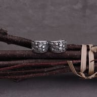 Pair of 316L stainless steel skull pattern ear cuffs on dark branches.