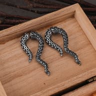 Pair of stainless steel octopus tentacle earrings displayed in a wooden box
