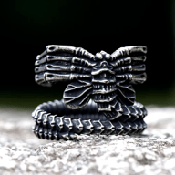 An oxidized stainless steel ring featuring a detailed, segmented creature design with an exoskeletal texture and multiple claw-like appendages, resting on a light grey textured surface.