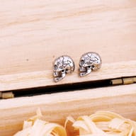 Pair of gothic cracked skull stainless steel stud earrings resting on a wooden box