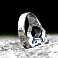 Top-down view of the 316L stainless steel Cry and Smile ring, emphasizing the contrast between the polished raised areas and the oxidized recesses of the masks.