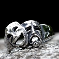 A 316L stainless steel ring with an antique and polished finish, featuring two side-by-side drama masks, one smiling and one crying.
