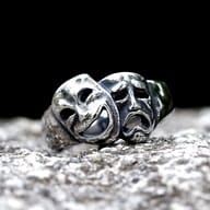 Macro shot of the crying drama mask on the stainless steel ring, detailing the tear drops and furrowed brow.