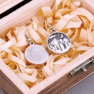 Detailed view of a single 316L stainless steel drop earring featuring a prominent mountain, forest, and crescent moon motif.