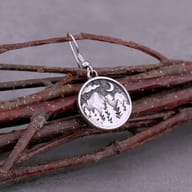 Angled close-up of the moon, clouds, and starry details above the mountain forest on a stainless steel earring.