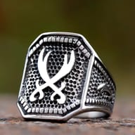 A polished silver-toned stainless steel ring with an octagonal shield face featuring two crossed Zulfikar swords on a pebbled textured background, with a raised dotted border, and patterned side bands.