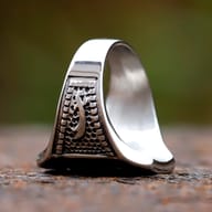 Detailed shot of the Zulfikar sword emblem on the men's and women's stainless steel ring, emphasizing the contrast between polished swords and textured background.
