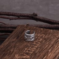 Stainless steel feather pattern ear cuff on rustic wood surface