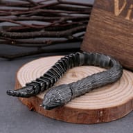 Detail of the bracelet's textured snake scale links, with blurred natural branches in the background, highlighting craftsmanship.