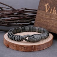 Close-up of the vintage-style snake chain bracelet with an Ouroboros snake head clasp, resting on a rustic wooden slice.