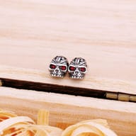 Close-up of a stainless steel skull stud earring highlighting detailed carved cranium and red eyes