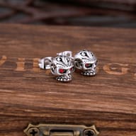 Pair of gothic stainless steel skull stud earrings with red crystal eyes resting on a wooden box