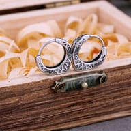 Pair of stainless steel Nordic geometric rune hoop earrings resting on a rustic wooden box