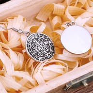 Detailed shot of a single 316L stainless steel Saint Benedict Medal drop earring on wood, emphasizing the CSPB inscription.
