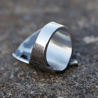 Polished stainless steel ring band and inner surface resting on a textured gray stone background.