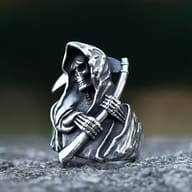 Close-up of an antiqued dark grey stainless steel ring featuring a hooded skeleton figure holding a sickle, with detailed skull face and skeletal hands.