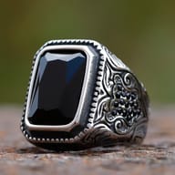 Three-quarter view of men's stainless steel signet ring featuring a faceted rectangular black stone and ornate filigree engraving