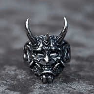 Detailed 316L stainless steel ring featuring a gothic demon skull design with polished horns, white eyes, intricate facial details, and dark oxidized recesses, on a dark textured background.