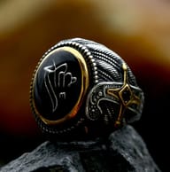 Angled close-up of Turkish signet ring on rock, highlighting black oval face, white symbol, and gold detail.