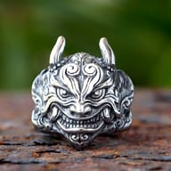 Full view of the stainless steel Oni mask ring on a rustic surface.