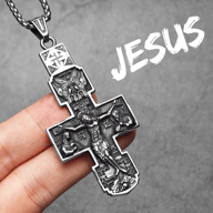 Full view of the stainless steel Orthodox crucifix pendant necklace, held by fingers, against a dark background.