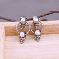 Side view of stainless steel double skull drop earrings highlighting the linked hoop connection