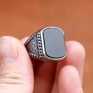 Full view of the robust stainless steel rectangle black stone ring against a rustic background.