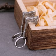 Two stainless steel Valknut rune axe drop earrings displayed in a rustic wooden box with wood shavings, on a dark stone surface.