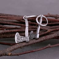 Two stainless steel Valknut rune axe drop earrings with detailed axe heads featuring Norse patterns, resting in a wooden box filled with light wood shavings.