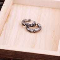 Pair of stainless steel octopus tentacle hoop earrings resting in a light wooden tray