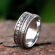Detailed view of the Elder Futhark rune pattern on the right side of the stainless steel ring band, highlighted against a soft green background.