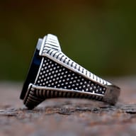 Side profile of the men's geometric black stone ring on a rustic surface
