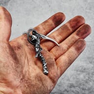 Close-up of the upper part of the skull scythe pendant, showing the skull and the curved scythe blade in stainless steel.
